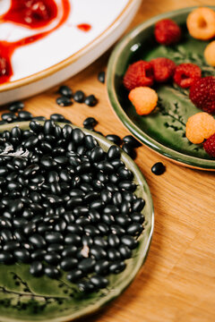 Black beans and fresh raspberries served on ceramic plates placed on a wooden table at daytime