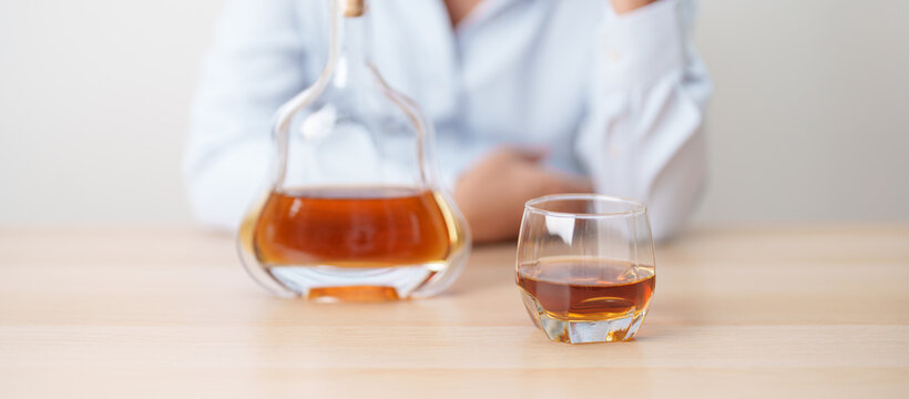 man with glass of cognac on table, suffering from alcohol addiction and alcoholism concept. depicting emotional distress, depression, substance abuse problem, unhealthy lifestyle and mental health