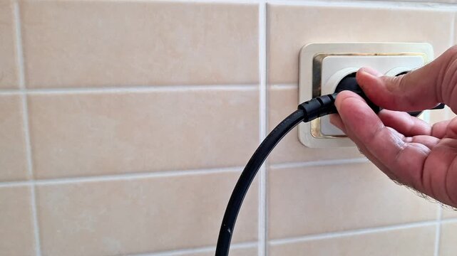 Hand plugs electrical power cord into wall socket, highlighting everyday energy use, home utility setup, and safe connection of devices to household electricity supply