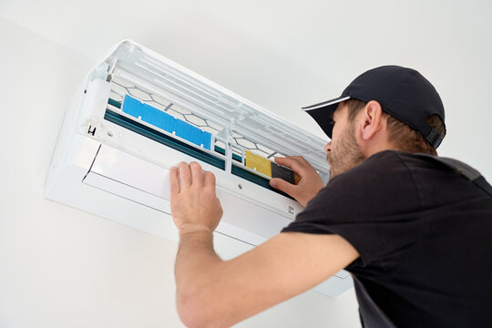 Man checking air conditioner filter in an open wall mounted split unit during maintenance. Concept of HVAC service, appliance care and seasonal cleaning