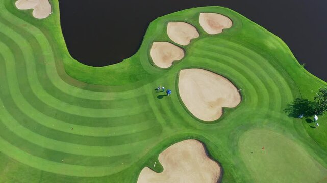 Professional golfer skillfully plays challenging green golf course featuring dramatic paw-shaped sand traps under dark, intense night sky for athletic sports photography.