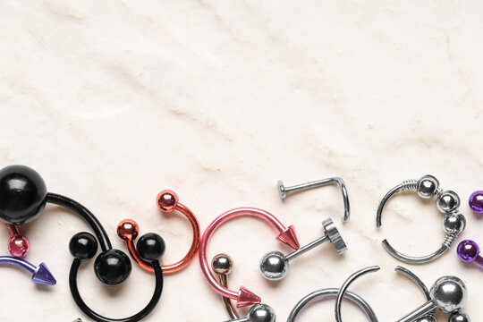 Assortment of colorful body piercing jewelry including barbells, rings, and studs on a marble background