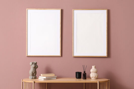 Two empty wooden frames on a dusty pink wall above a console table with home decor items