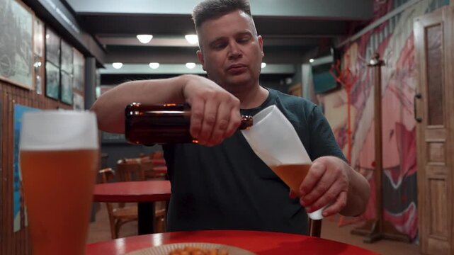 Man sitting at a bar pouring beer into a glass, bartending or serving drink, pub atmosphere.