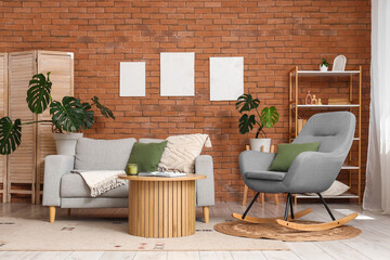 Modern living room interior with gray sofa, rocking chair, and monstera plants against a brick wall © Pixel-Shot