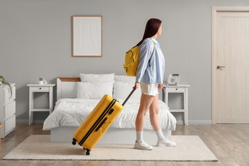 Plakat Young woman with a yellow suitcase and backpack walking through a modern hotel room, ready for travel and adventure