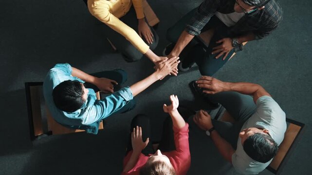 Top down aerial view of smart business people putting hands together to celebrate successful project while sitting chair circle. Aerial view of skilled marketing team making stack of hands. Symposium.