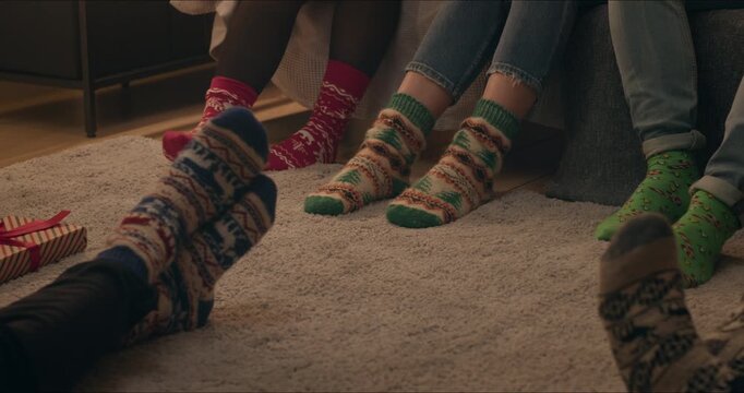 Close-up of feet in colorful knitted Christmas socks resting on a soft rug beside wrapped holiday gifts.