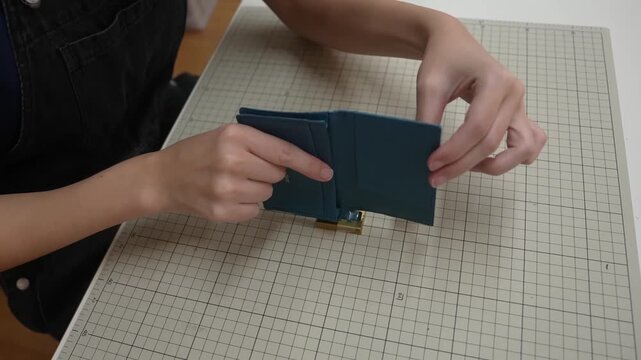 Hands fold finished trifold leather wallet closed for final inspection