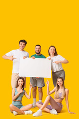Fototapeta premium Group of diverse young people holding a blank white banner and pointing, offering copy space for advertising or message on a yellow background