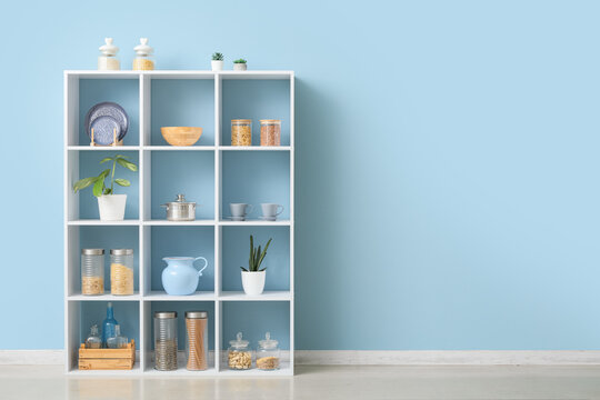 White modular shelving unit with kitchenware and food storage containers against a light blue wall
