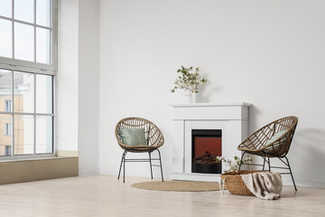 Obraz premium Interior of light living room with blooming branches in vases, fireplace and armchairs