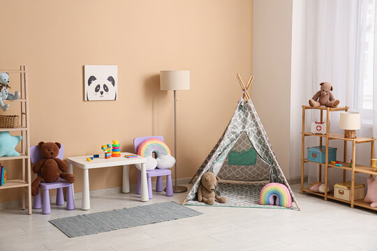 Interior of childrens room with play tent, lamp, play table and many toys in shelving units near beige wall