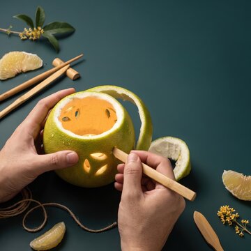 Hands carving a pomelo lantern for Mid Autumn Festival celebration with chopsticks and fruit slices