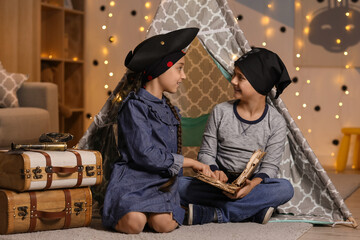 Cute children dressed as pirates reading adventure book at home in evening © Pixel-Shot