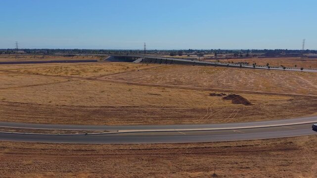 Descending and Reversing Aerial Drone Shot Over Dirt Field With Freeway Overpass Power Lines and Traffic in Fresno California