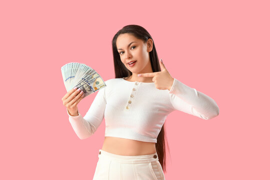 Young woman pointing at dollar banknotes on pink background