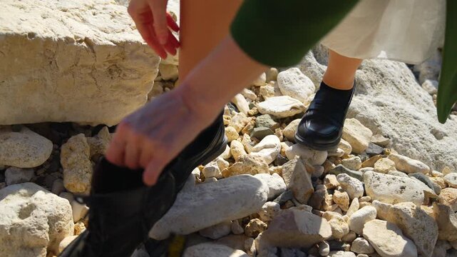 Shoes rocks fashion woman hands picking up stylish black leather boot from stony ground while wearing black loafers on a sunny day
