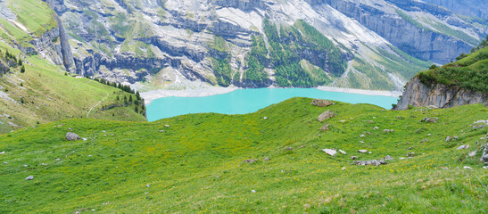 Obraz premium Scenic landscape of Oeschinensee or turquoise Oeschinen Lake in summer under blue sky with wildflowers and Stunning Swiss Alps. Spectacular green meadow hiking trail view, Kandersteg, Switzerland