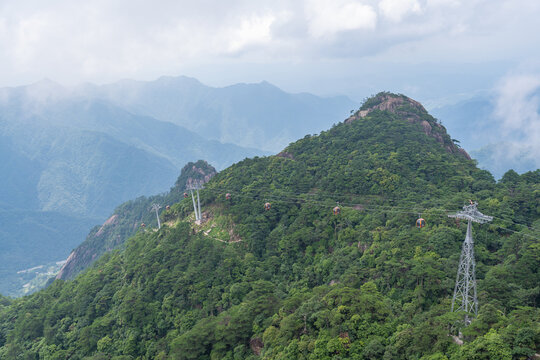 A scenic view shows a cable car system moving over the lush green mountains of Sanqingshan Mountain in Jiangxi province of China during a cloudy summer day