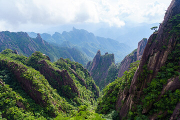 A scenic view shows the dramatic granite peaks and lush green vegetation of Sanqingshan Mountain located in the Jiangxi province of China during a clear summer day © AS_SleepingPanda