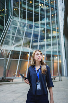 Businesswoman wearing id badge holding a folder standing outside modern office building