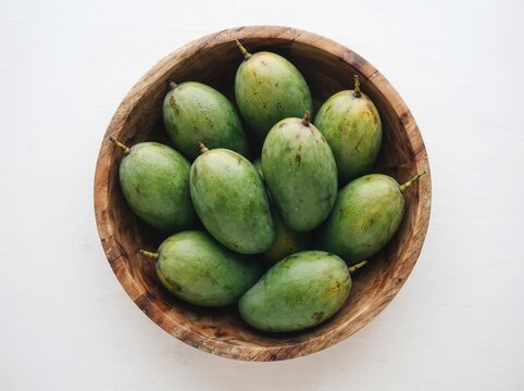 Fresh green raw mangoes in a wooden bowl on white background top view.