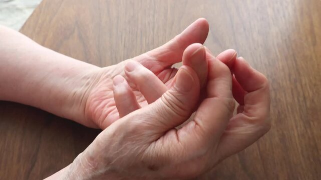 A senior woman's hand touching the knuckles of her fingers on a wooden table.