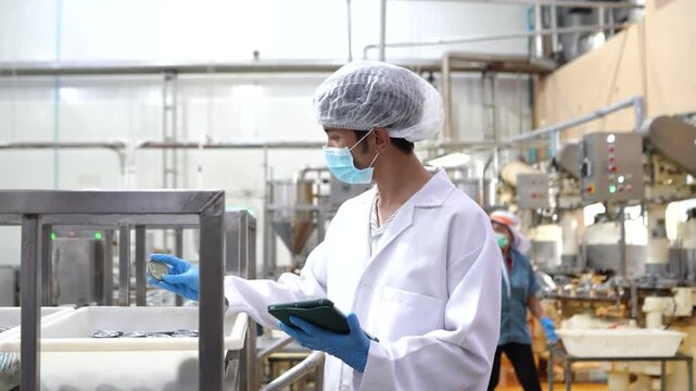 Food quality inspector checking canned fish production with digital tablet on processing line. Food safety, quality control, manufacturing inspection, seafood factory operations.