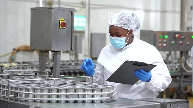 Food quality inspector checking canned fish production with digital tablet on processing line. Food safety, quality control, manufacturing inspection, seafood factory operations.