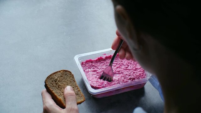 Woman eating traditional herring fur coat layered salad from plastic container, store bought ready meal. Beetroot salad as convenience food. Woman eating herring fur coat salad from plastic container