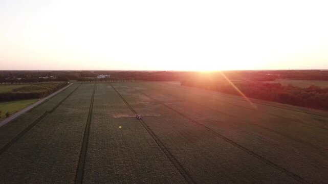 drone shot at sunset showing a farmer driving across his field to irrigate the land, captured in backlight with beautiful lines in the landscape, Drenthe, Netherlands