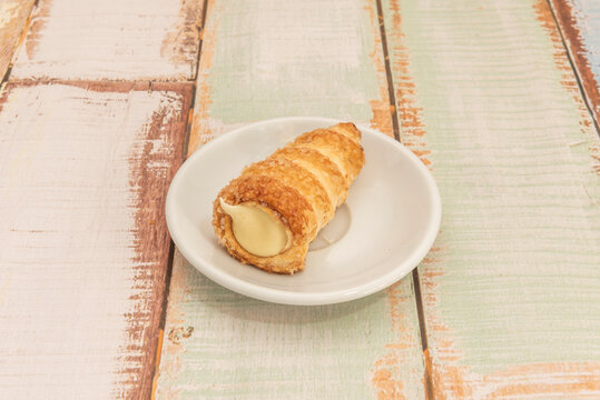 Ridged puff pastry cone dusted with coarse sugar, spilling smooth cream from its tip on a rustic wooden table.