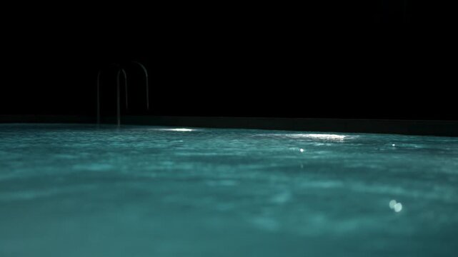 Swimming pool with clear blue water and bright underwater lights at night.