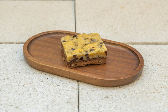 Layered brookie bar with cookie dough topping over a fudgy brownie base, plated on a wooden board.