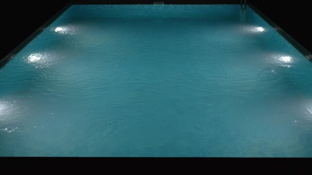 Swimming pool with clear blue water and bright underwater lights at night.