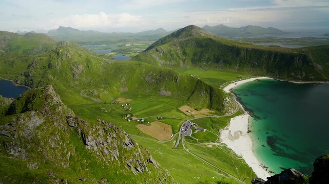 Steep coastal hills drop to a white sand bay and scattered farmsteads with turquoise water and winding roads below.