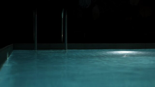 Swimming pool with clear blue water and bright underwater lights at night.