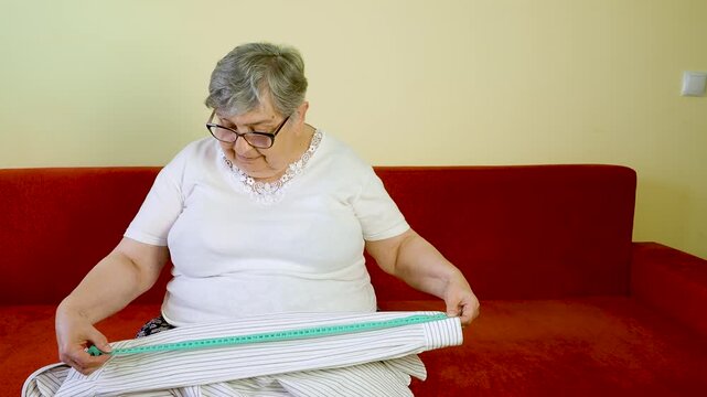 Senior Woman Measuring Fabric With Tailor Tape While Sewing at Home