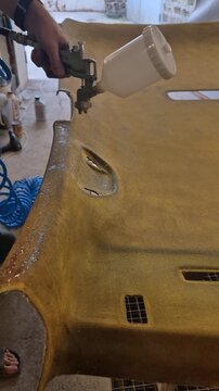 Headliner car repair, worker sprays adhesive onto vehicle ceiling panel for restoration process