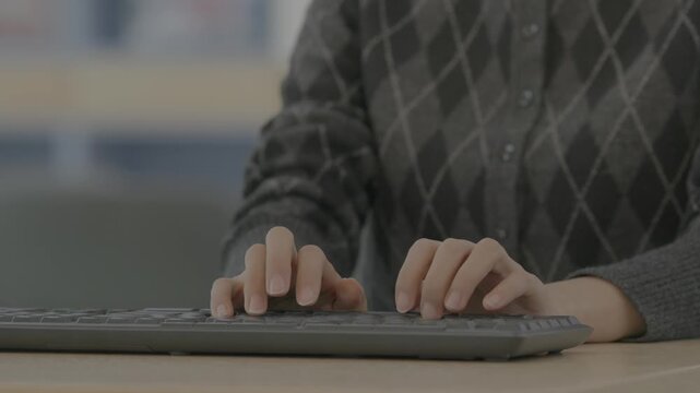A close-up of a person's hands on a dark keyboard with fingers bent in an awkward position suggesting work-related wrist strain.