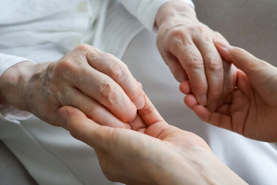 Caregiver gently holding an elderly woman's hands at home