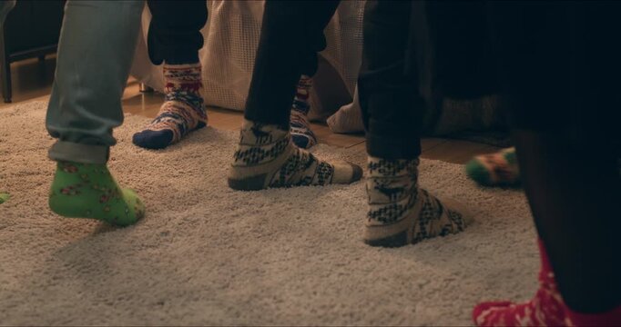 Close-up of feet in cozy patterned Christmas socks standing on a soft rug during a warm holiday gathering at home.