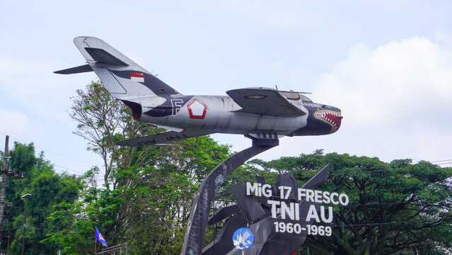 A display of a vintage MiG-17 Fresco fighter jet, formerly operated by the Indonesian Air Force (TNI AU), mounted on a pedestal as a monument in a public space in Malang, Indonesia. 
