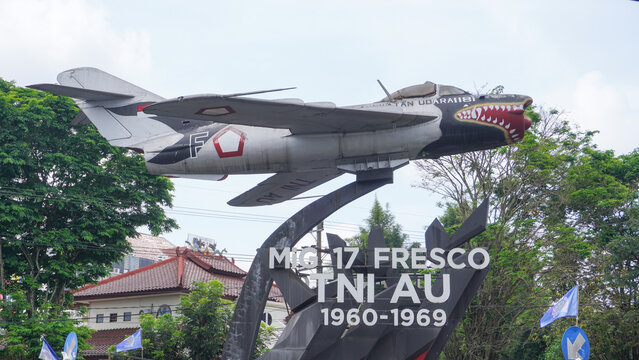 A display of a vintage MiG-17 Fresco fighter jet, formerly operated by the Indonesian Air Force (TNI AU), mounted on a pedestal as a monument in a public space in Malang, Indonesia. 