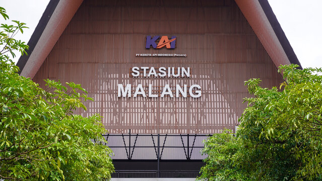 Modern facade of Malang railway station building with green trees and parking area in East Java, Indonesia.