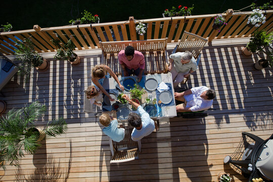Above shot of family eating at barbecue party dinner on patio, little girl eating roasted corn and enjoying it.