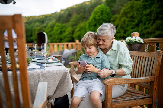 Little boy with his grandmother looking in smartphone during bbq party.