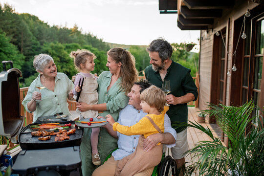 Multi generation family grilling outside on patio in summer during garden party