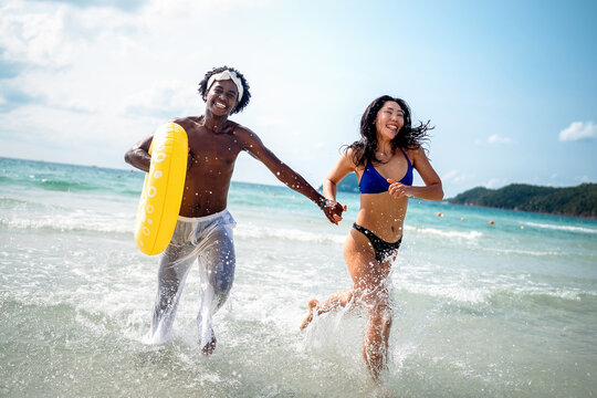 Friends, diverse couple having fun with colorful inflatable rings at the seaside